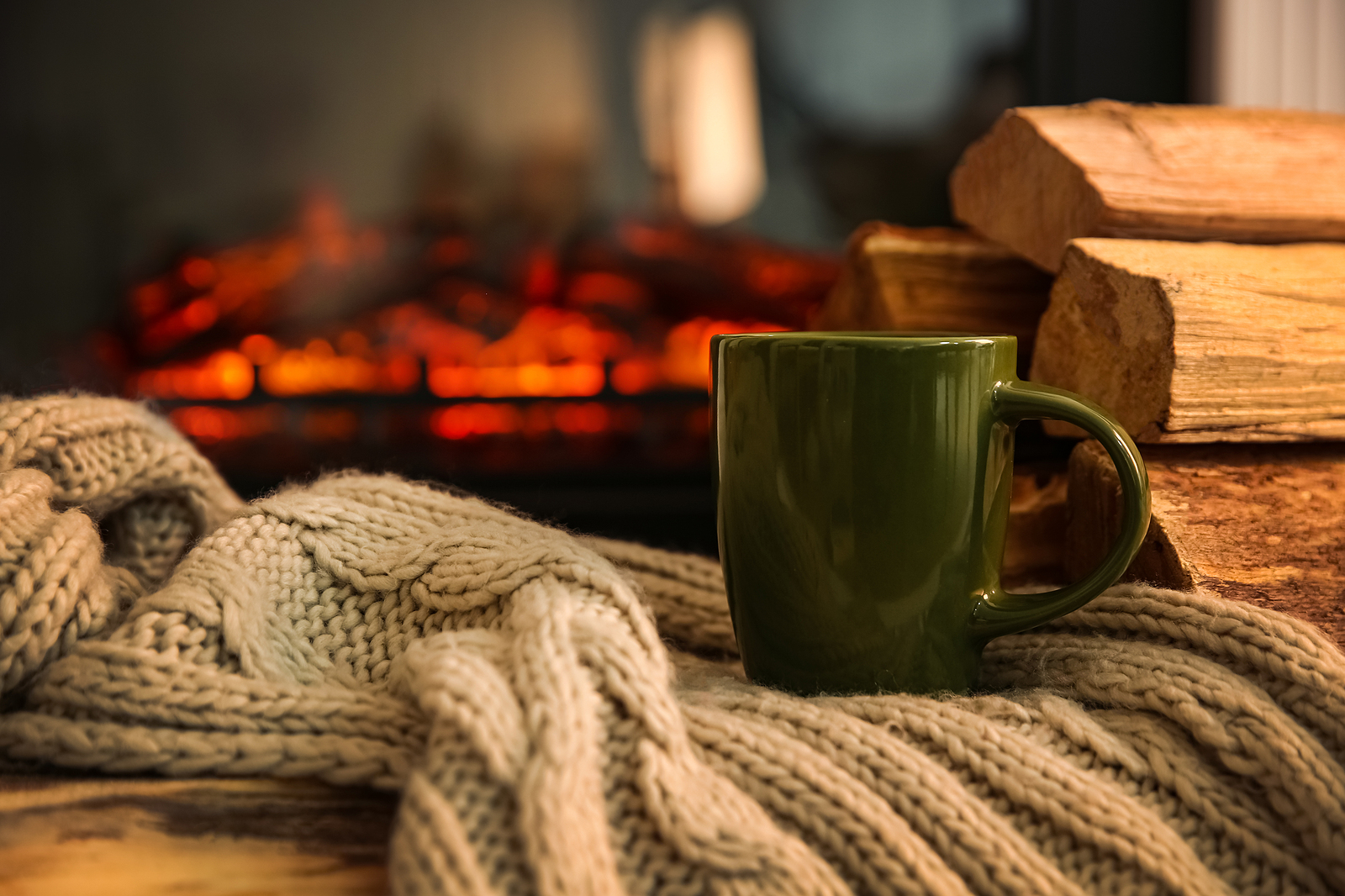 Green Cup With Hot Drink And Blanket On Table Against Fireplace