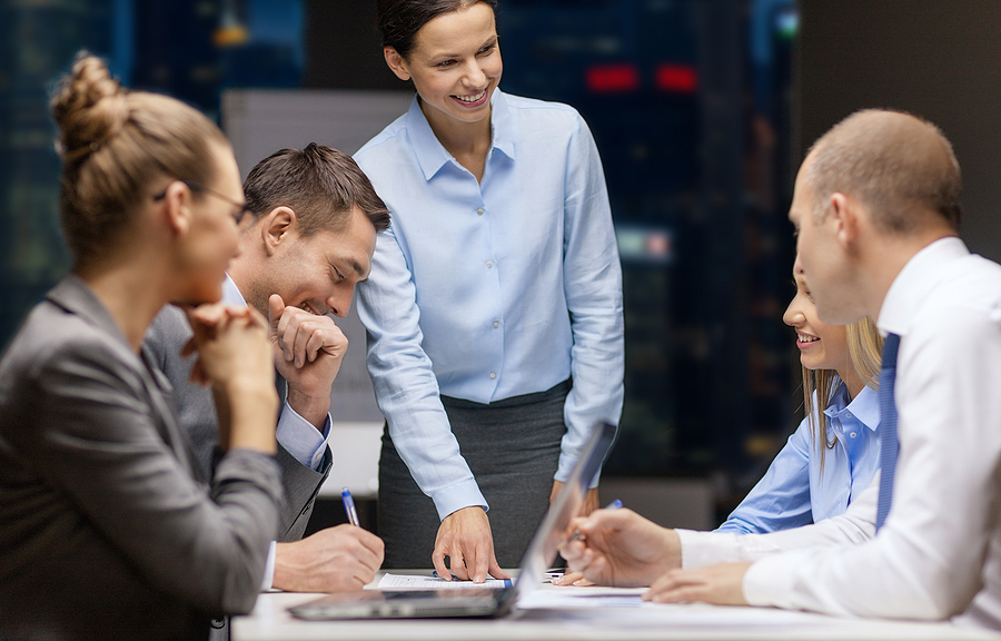 business, technology, people, deadline and team work concept - smiling female boss talking to business group at night office background