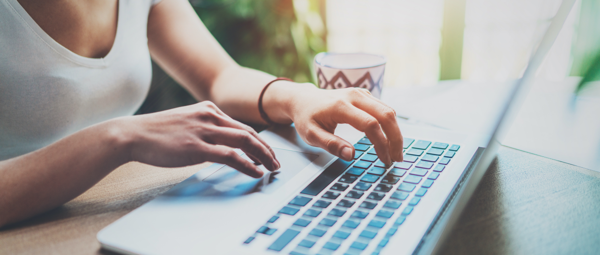 Young woman working at home on modern computer while sitting at the wooden table.Female hands typing on laptop keyboard.Concept of young modern people using mobile devices at home.Blurred background