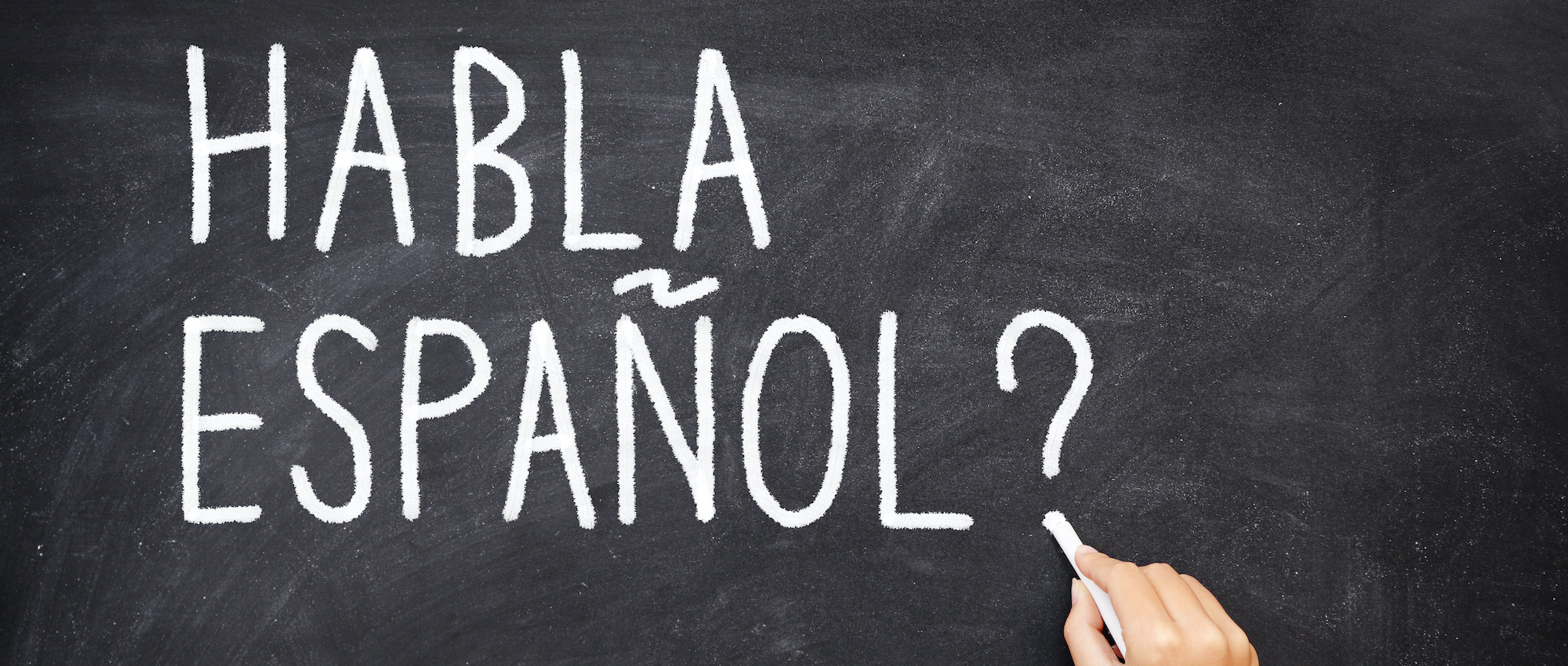 Spanish language learning concept image. Teacher or student writing "habla espanol" on blackboard during spanish language course class.